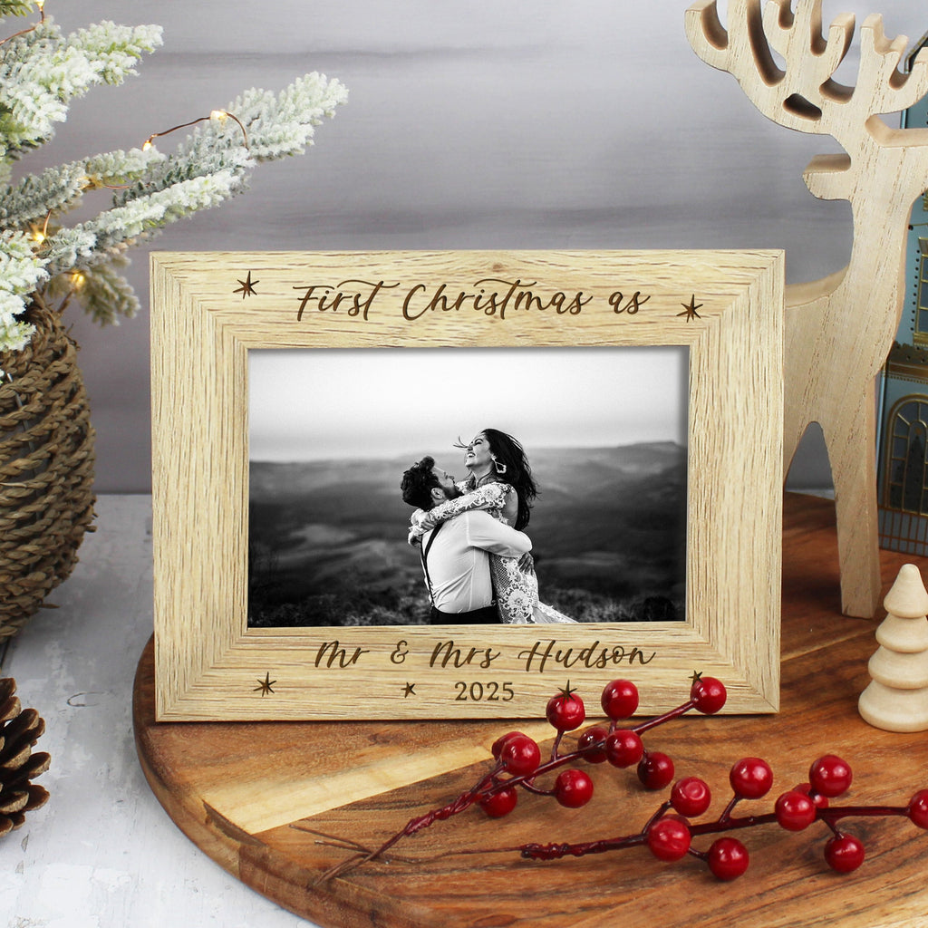 Wooden photo frame with 'First Christmas as' engraving on a decorative table with festive items.