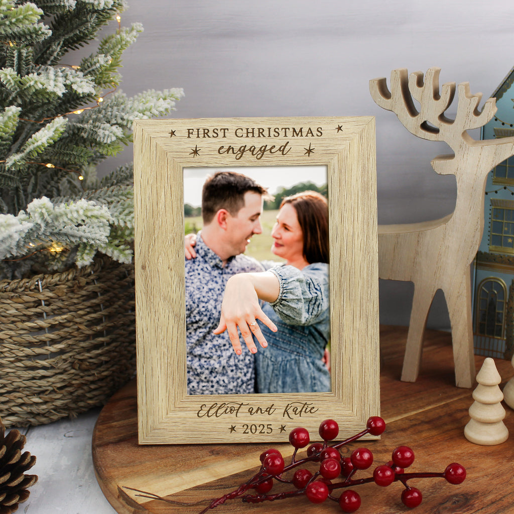 Wooden photo frame with a couple's photo and 'First Christmas engaged' text, surrounded by Christmas decor.