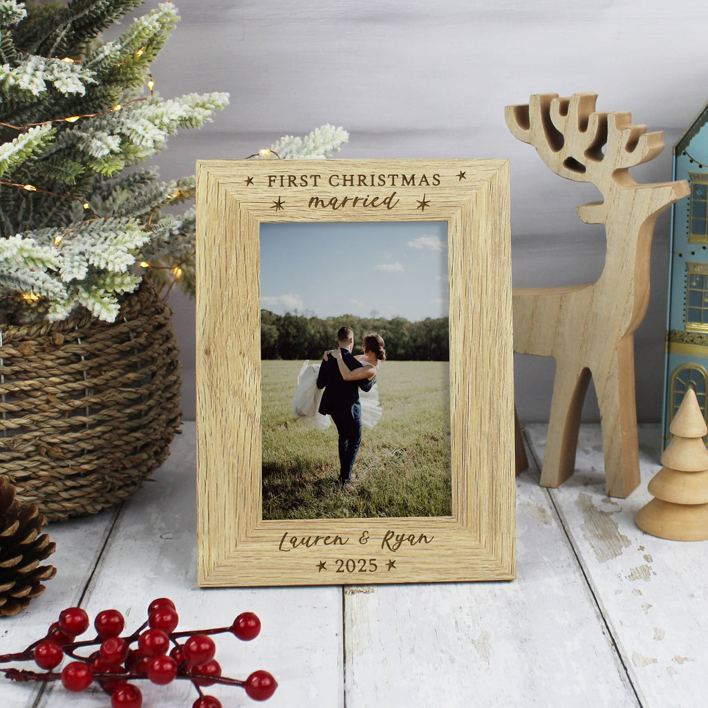 Wooden photo frame with a couple's picture, surrounded by Christmas decorations on a wooden surface.