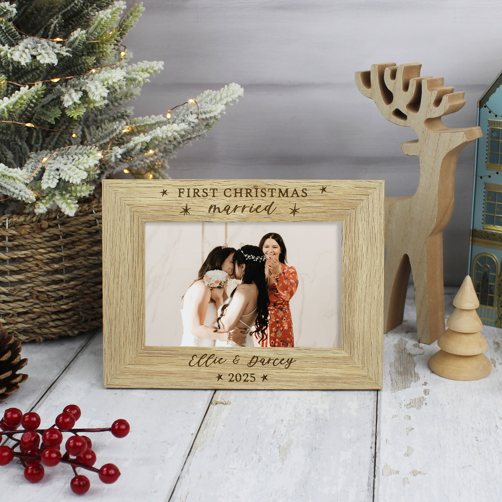 Wooden photo frame with 'First Christmas married' engraving, placed on a festive background with a Christmas tree and decorations.