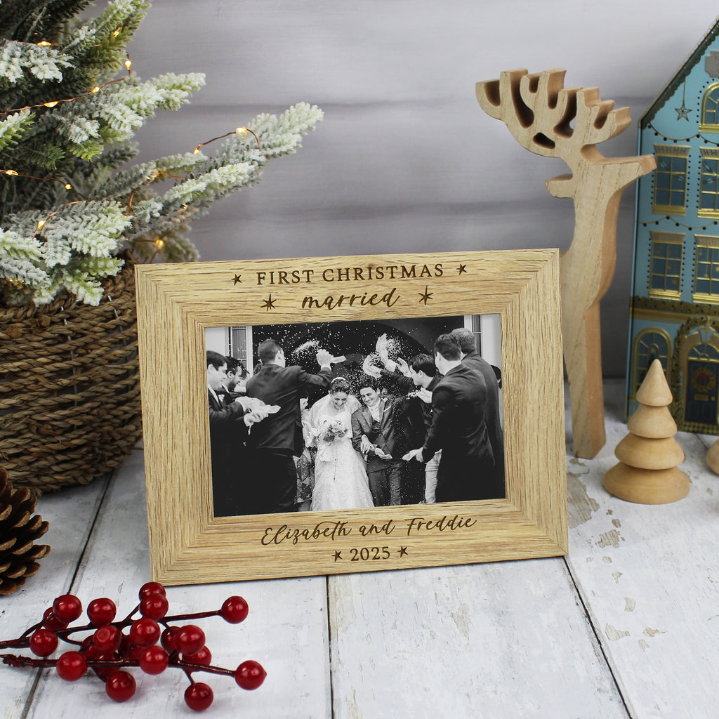 Wooden photo frame with 'First Christmas married' engraving, surrounded by festive decorations.