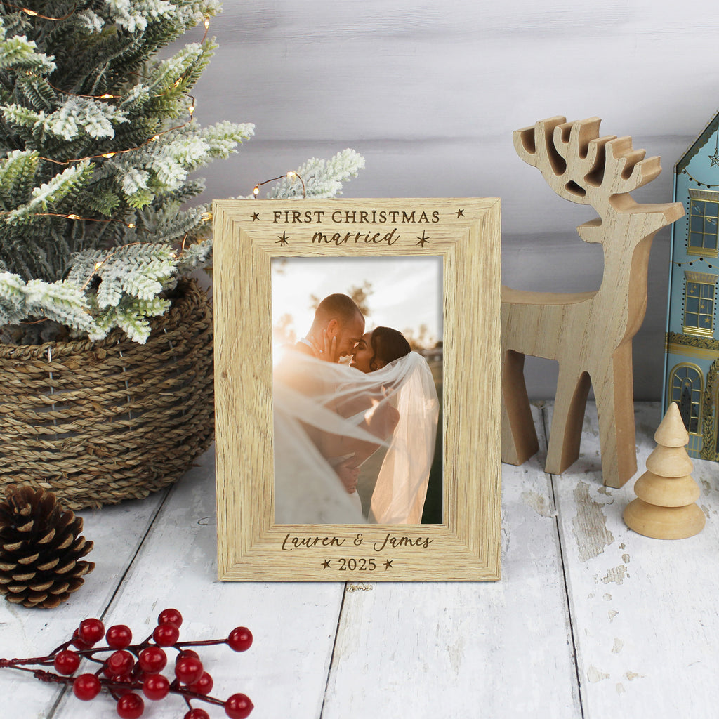 Wooden photo frame with 'First Christmas married' text, surrounded by Christmas decor on a wooden surface.