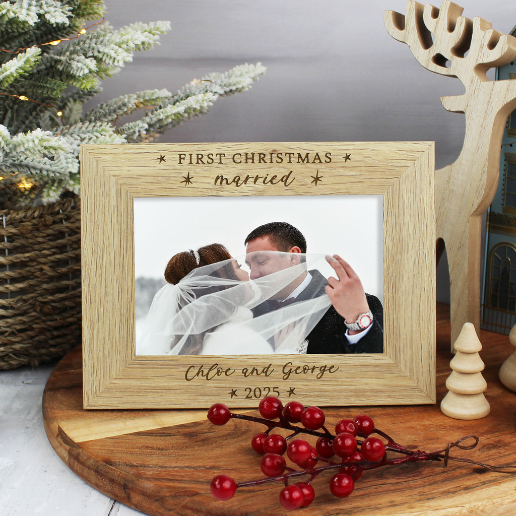 Wooden photo frame with 'First Christmas married' engraving, placed on a table with festive decorations.