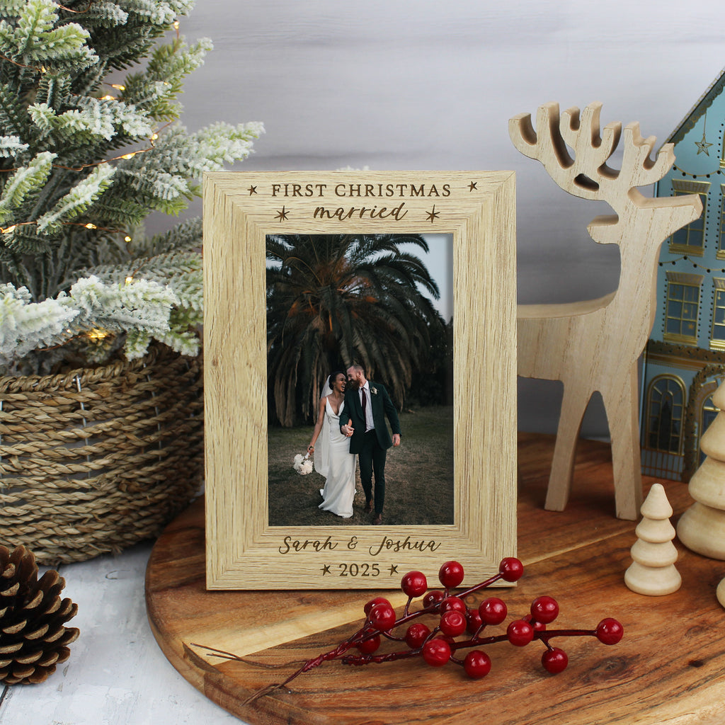 Wooden photo frame with 'First Christmas married' engraving, placed on a wooden surface with festive decorations.