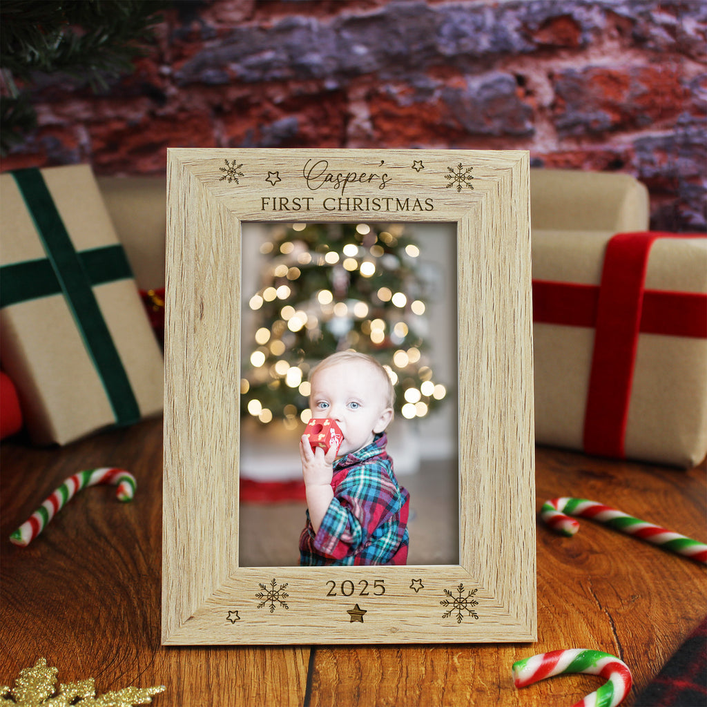 Wooden photo frame with 'Casper's First Christmas' engraving, placed on a festive background with a blurred Christmas tree and presents.