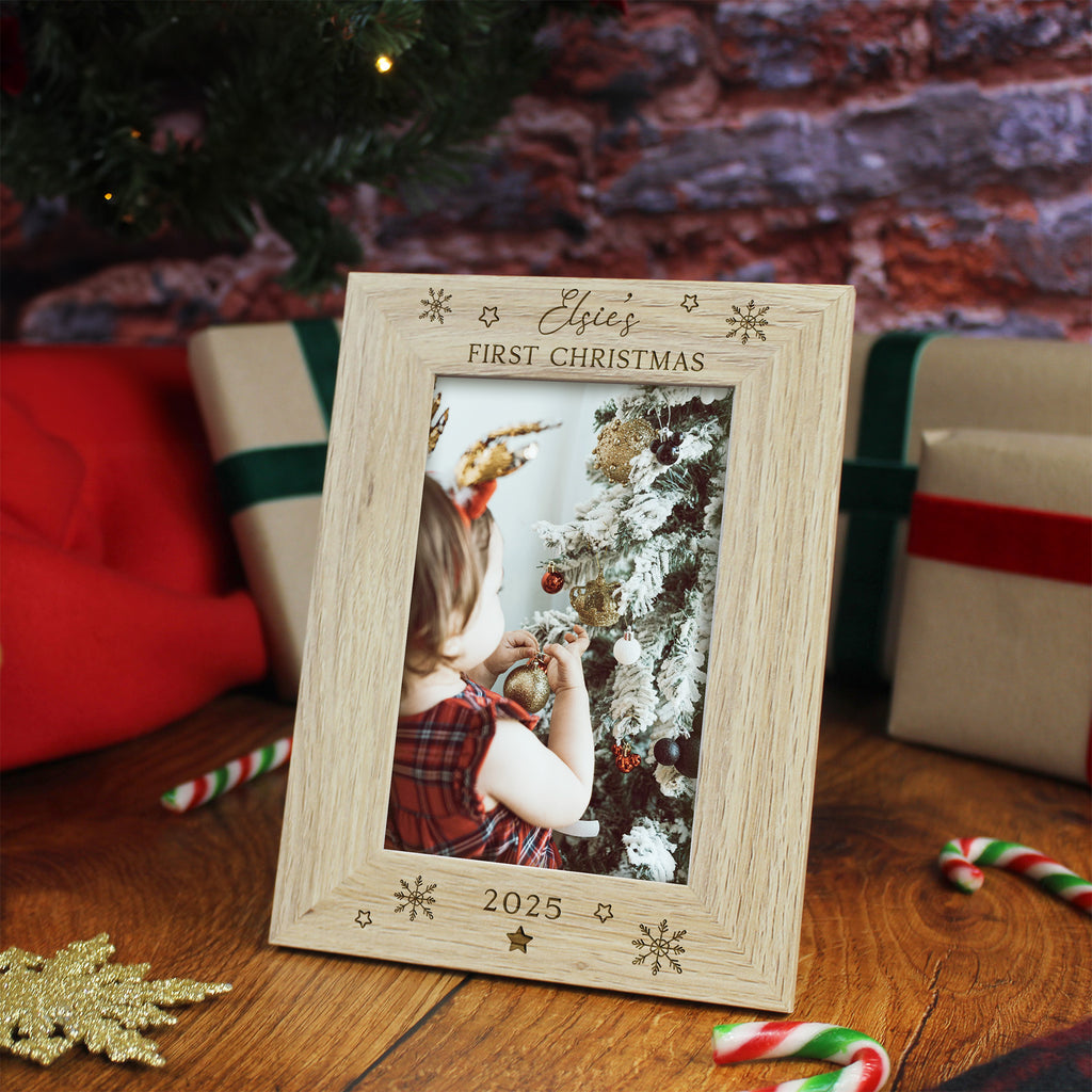 Wooden photo frame with 'Eloise's First Christmas 2025' text, placed on a wooden surface with Christmas decorations.