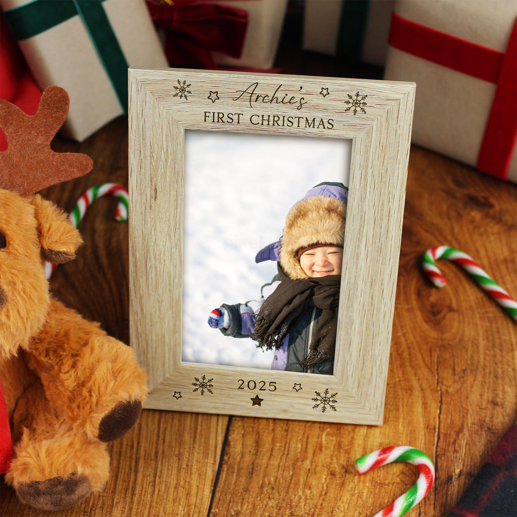 Personalized photo frame for 'Archie's First Christmas 2025' with a child's photo, surrounded by Christmas decorations on a wooden surface.