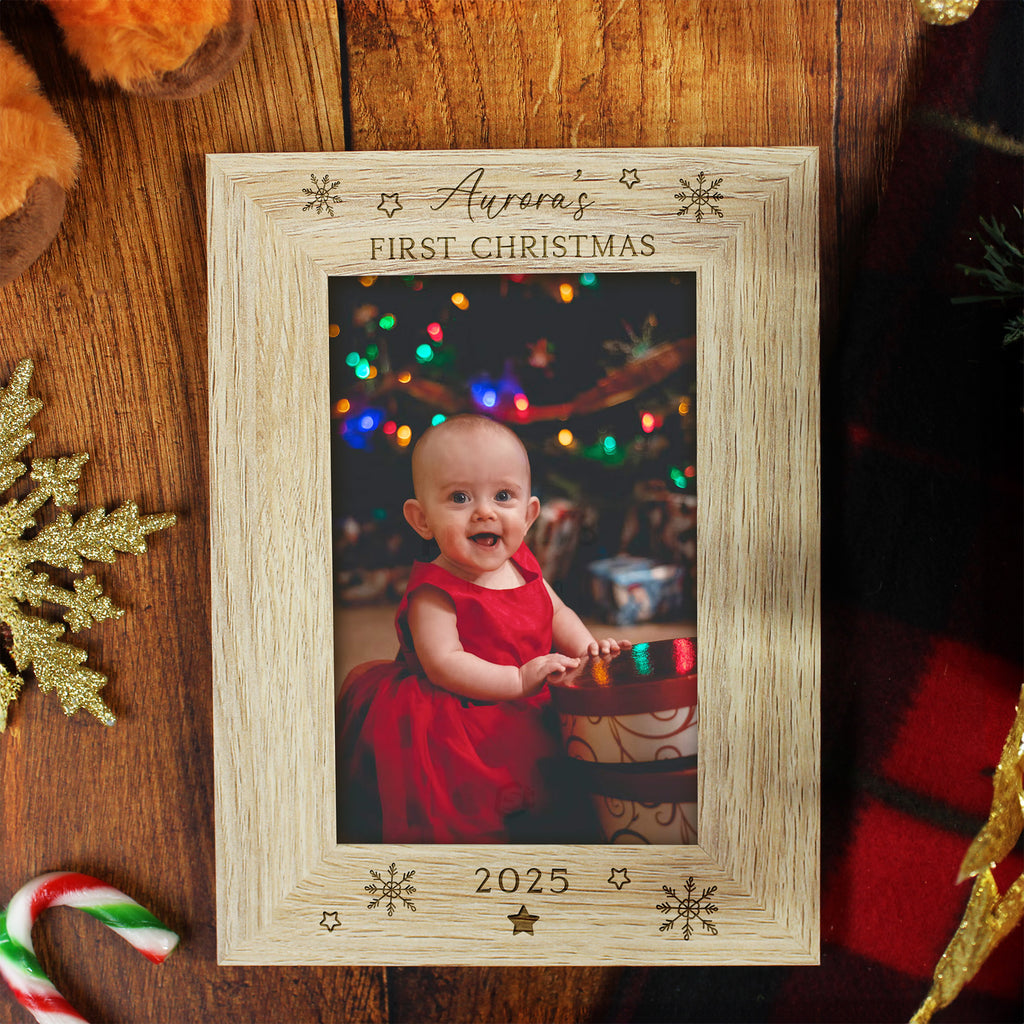 Wooden photo frame with a Christmas-themed picture of a baby, surrounded by festive decorations on a wooden surface.