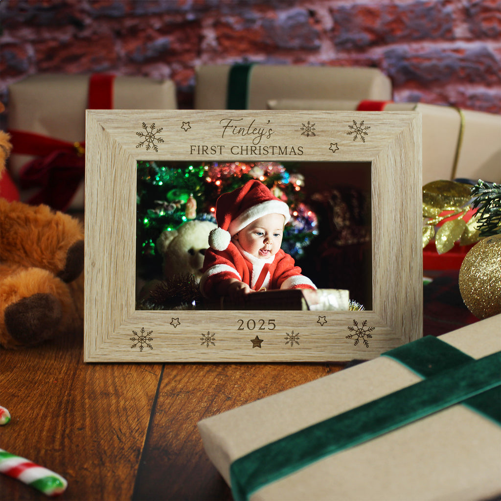 Wooden photo frame with 'Finley's First Christmas 2025' text, surrounded by Christmas decorations and gifts.