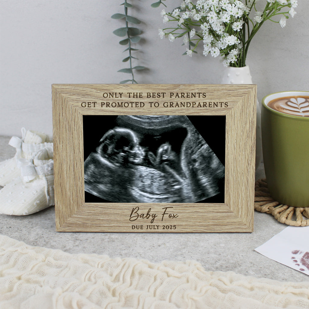 Wooden picture frame with ultrasound photo and engraved text on a surface with a cup and flowers in the background.
