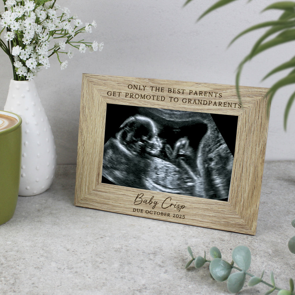 Wooden picture frame with ultrasound photo and engraved text on a surface with flowers and a mug.