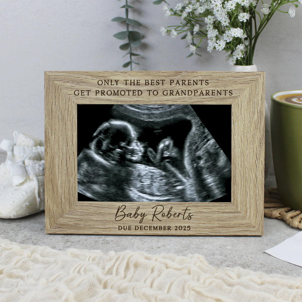 Wooden frame with ultrasound photo and engraved text on a surface with a cup and flowers in the background.