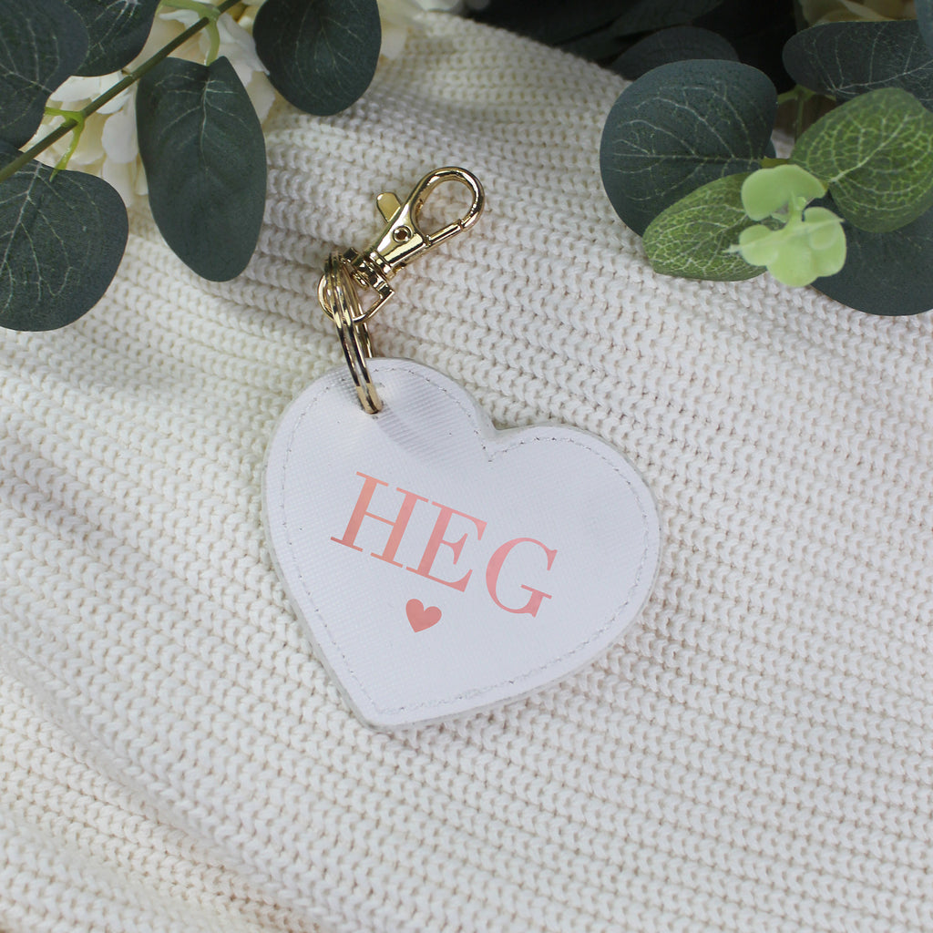 Heart-shaped keychain with 'HEG' on a textured surface with green leaves.