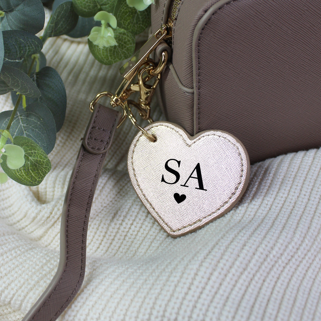 Heart-shaped keychain with 'SA' initials attached to a brown handbag on a textured surface.