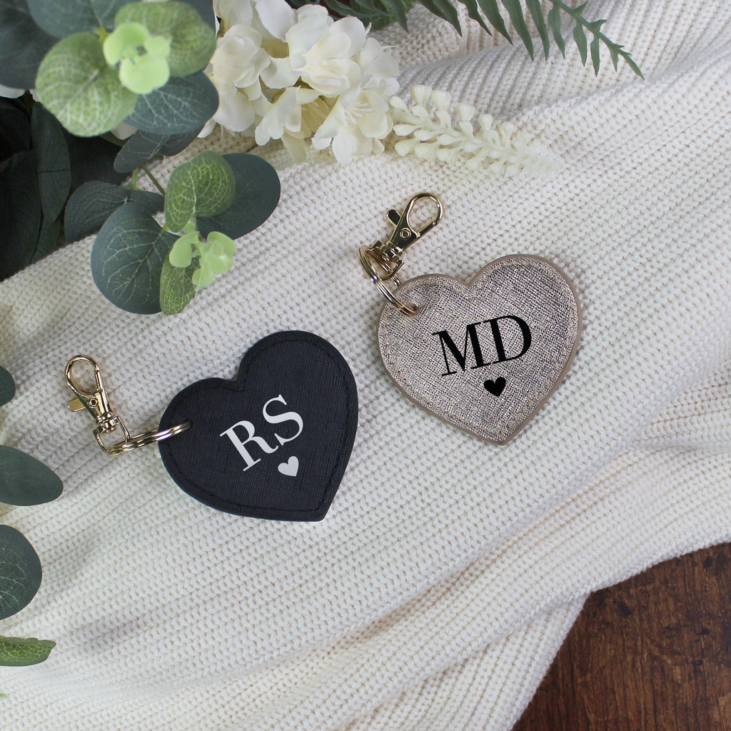Heart-shaped keychains with initials 'RS' and 'MD' on a textured surface with greenery.