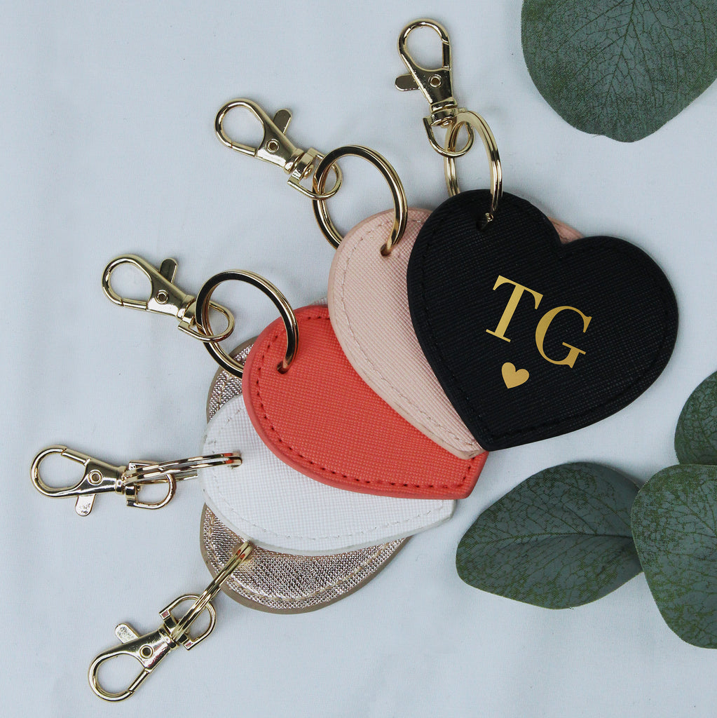 Heart-shaped keychains in black, red, and pink with 'TG' initials on a light gray background.