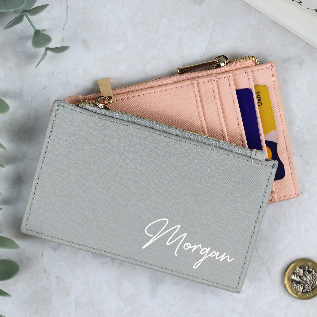 Gray wallet with 'Morgan' engraving on a light surface with a pink wallet and cards.