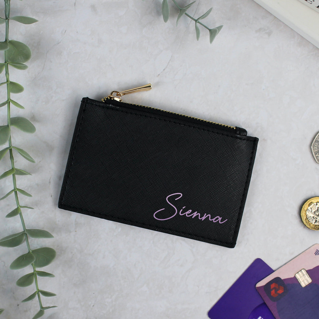 Black pouch with 'Sienna' embroidery on a light gray surface with cards and coins.