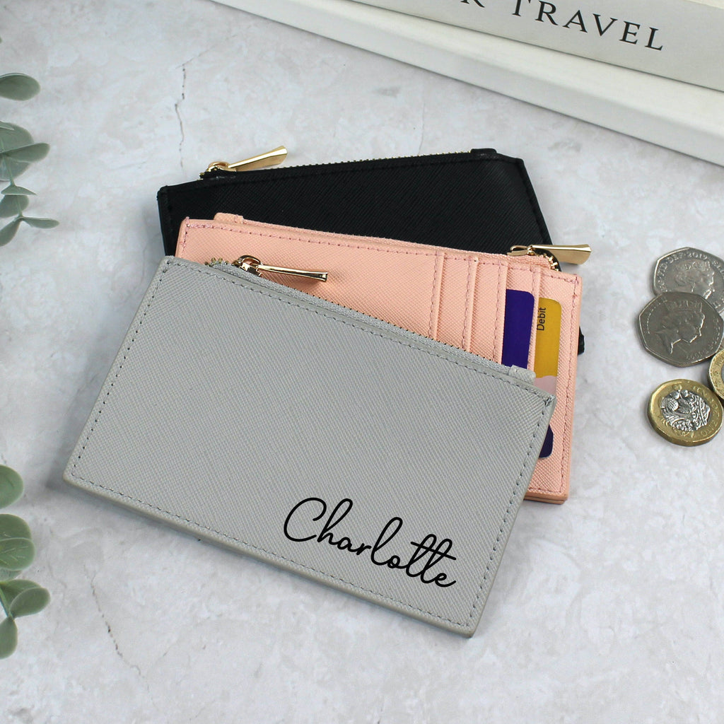 Gray wallet with 'Charlotte' branding on a light surface with coins and a plant.