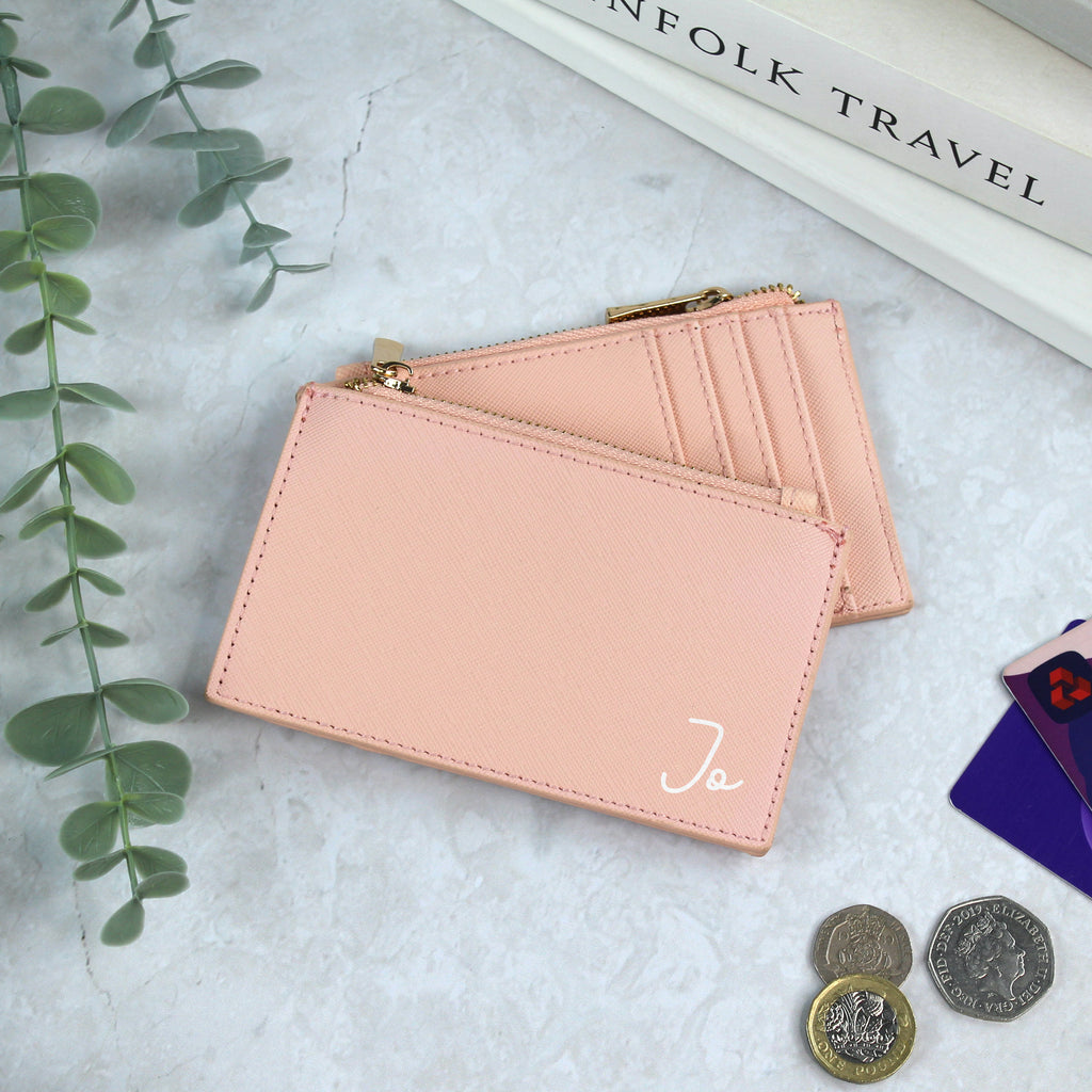 Two pink card holders on a marble surface with coins and a plant.
