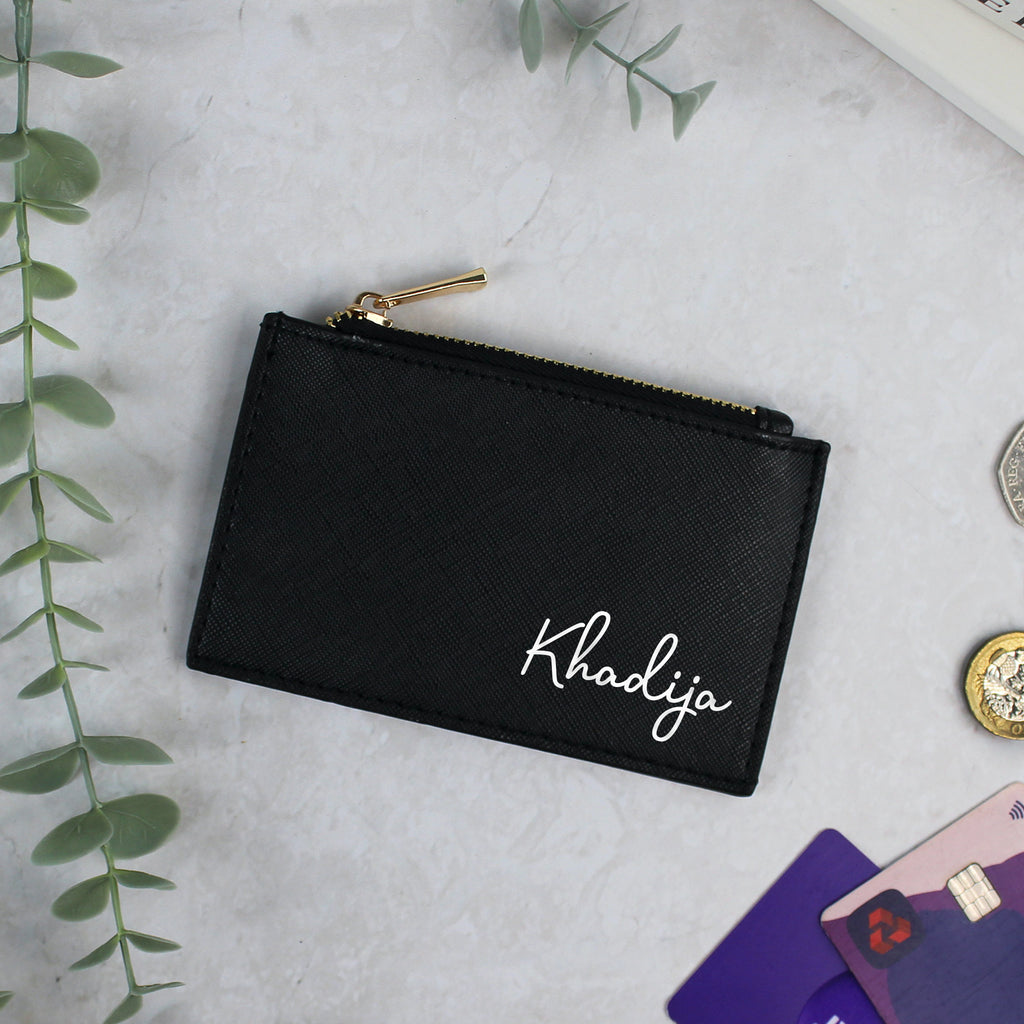 Black pouch with 'Khadija' branding on a light gray surface with cards and coins.