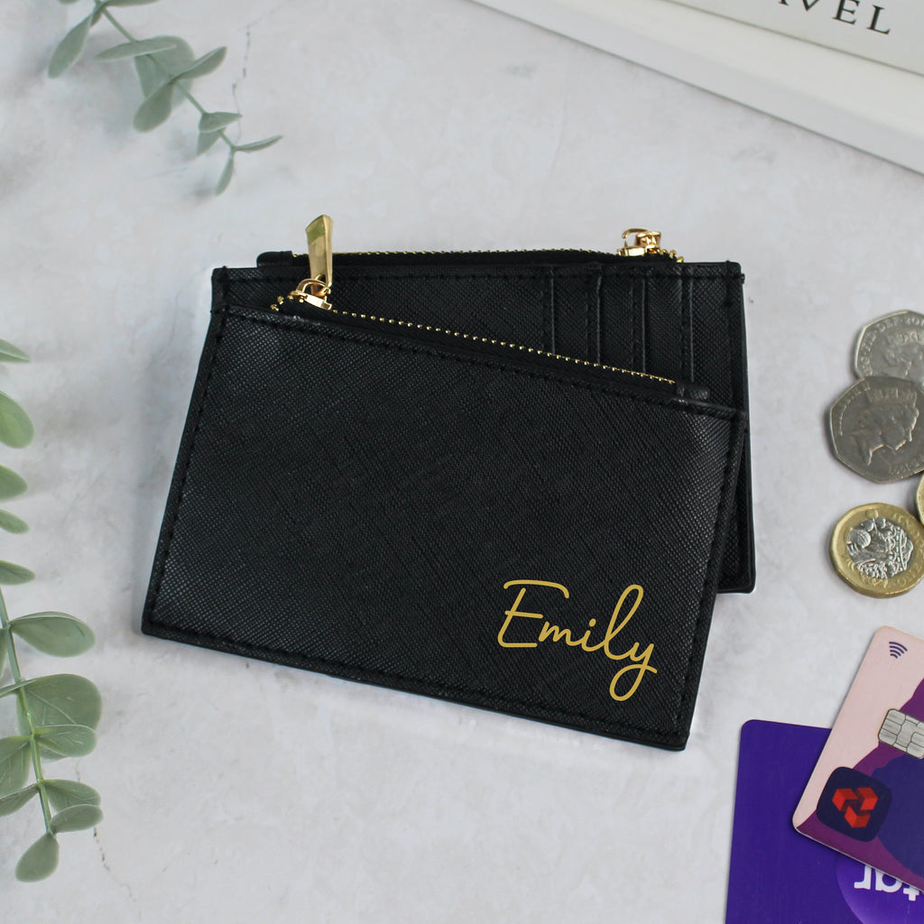 Black wallet with 'Emily' engraving on a light gray surface with coins and cards.