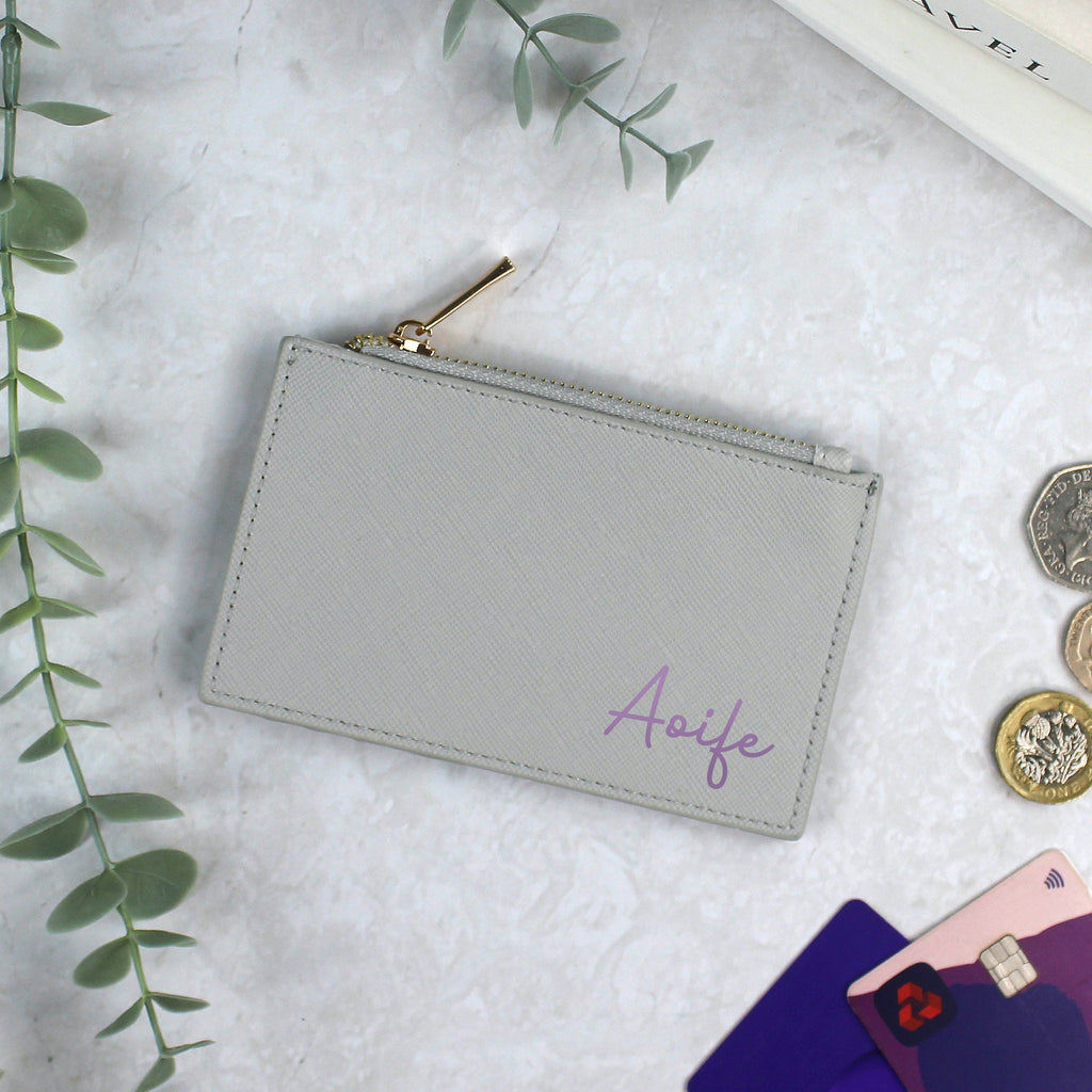 Gray pouch with 'Aoife' embroidery on a light gray surface with coins and cards.