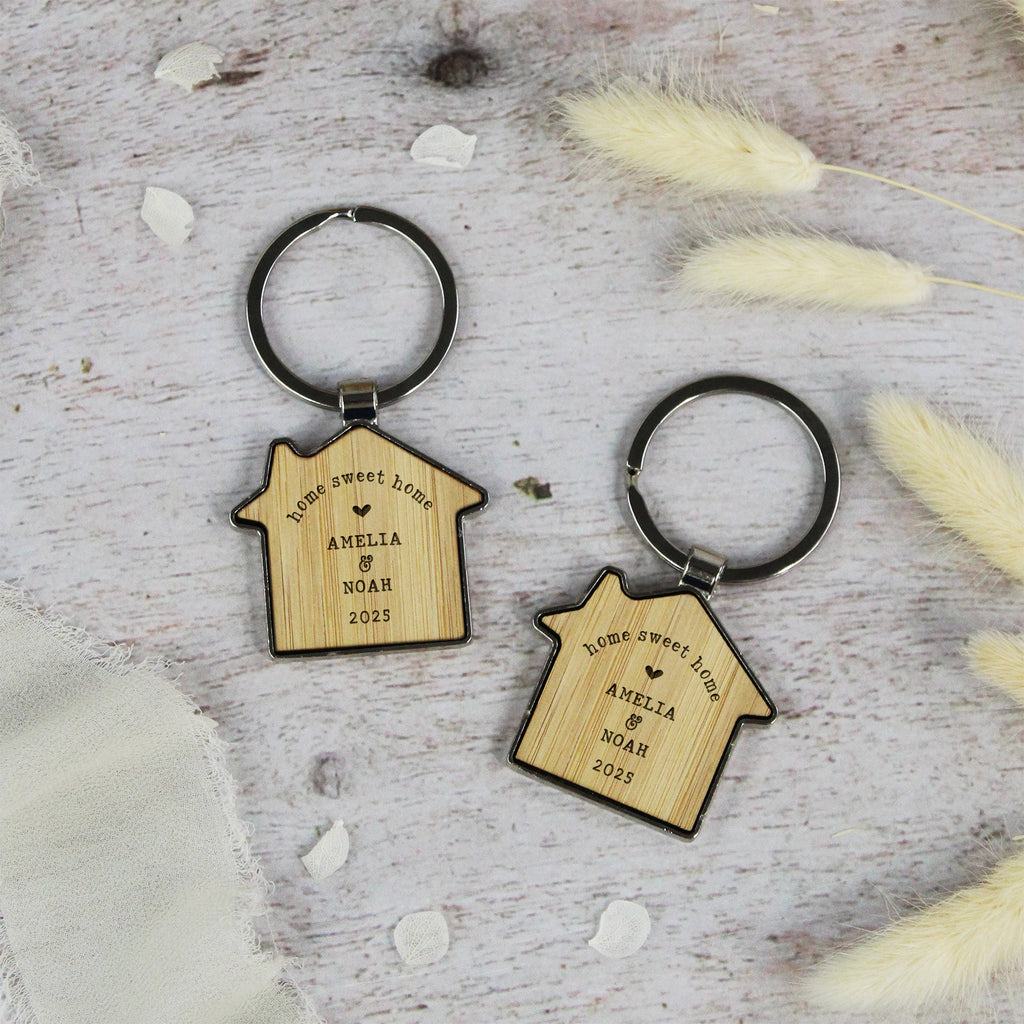 Two wooden house-shaped keychains with engraved text on a light wooden surface.