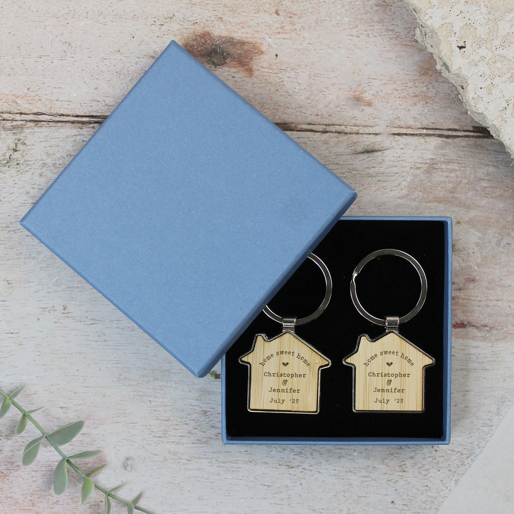 Two house-shaped keychains in a blue box on a wooden surface.