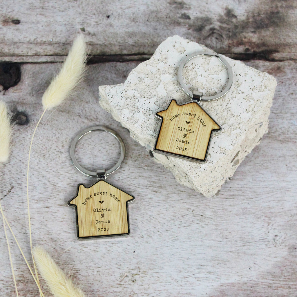 Two wooden house-shaped keychains with engraved text on a rustic wooden surface.