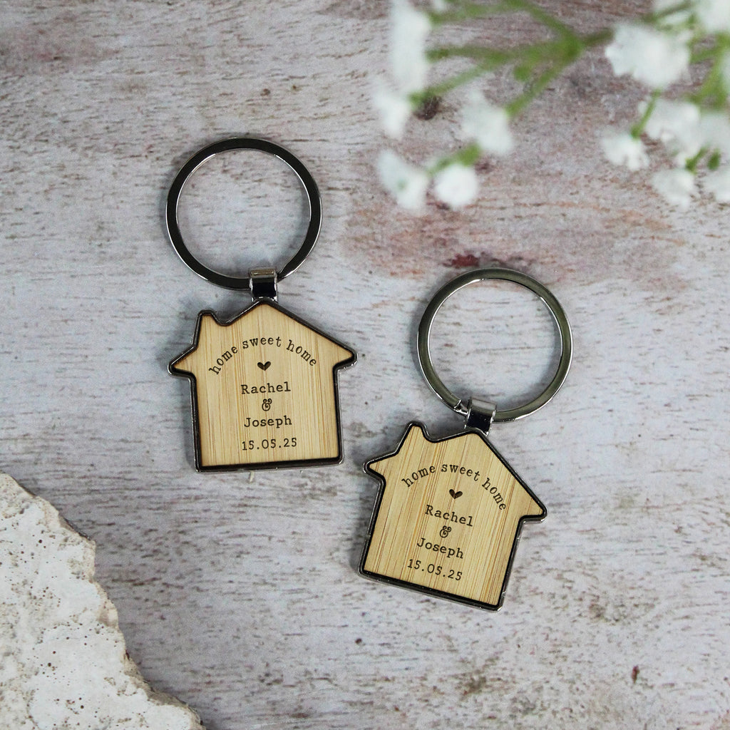 Two house-shaped wooden keychains with engraved text on a rustic surface.