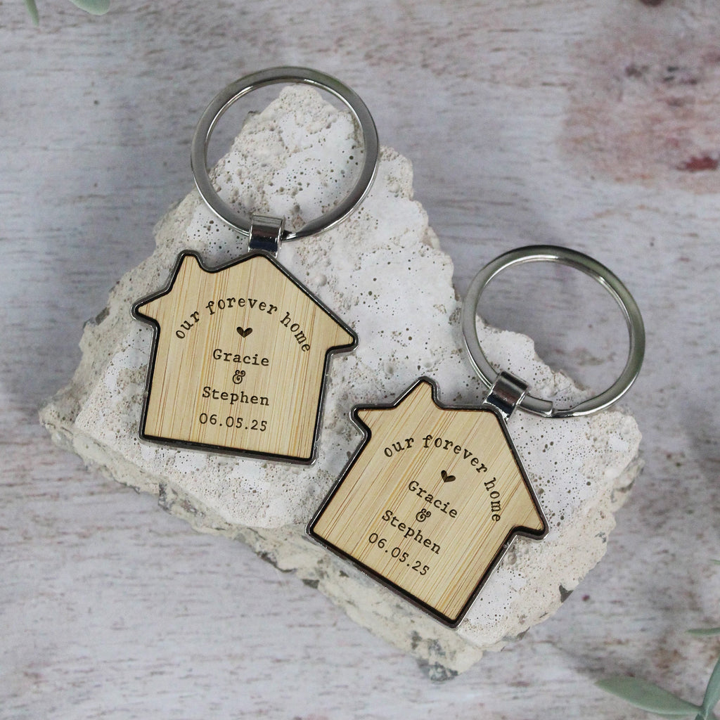 Two wooden keychains shaped like houses with engraved text on a stone surface.