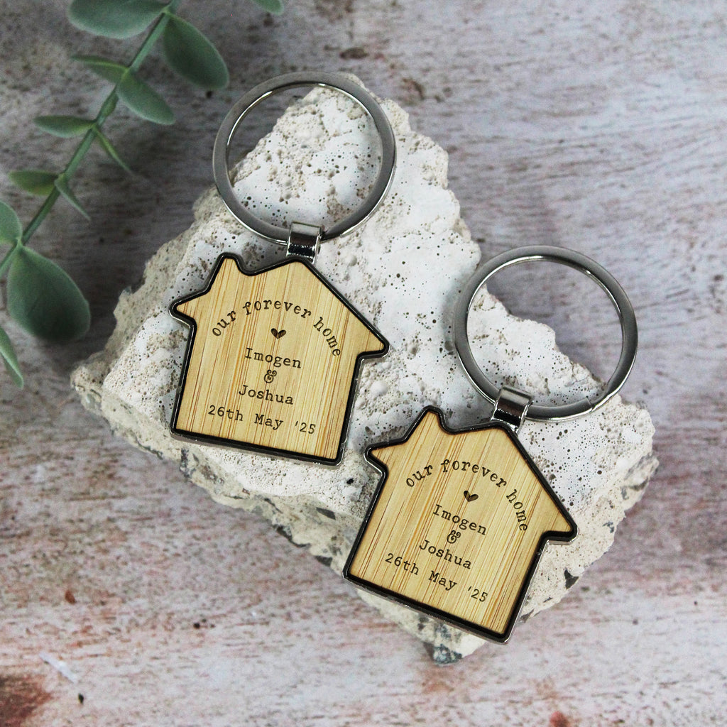 Two wooden house-shaped keychains on a stone surface with a plant in the background.
