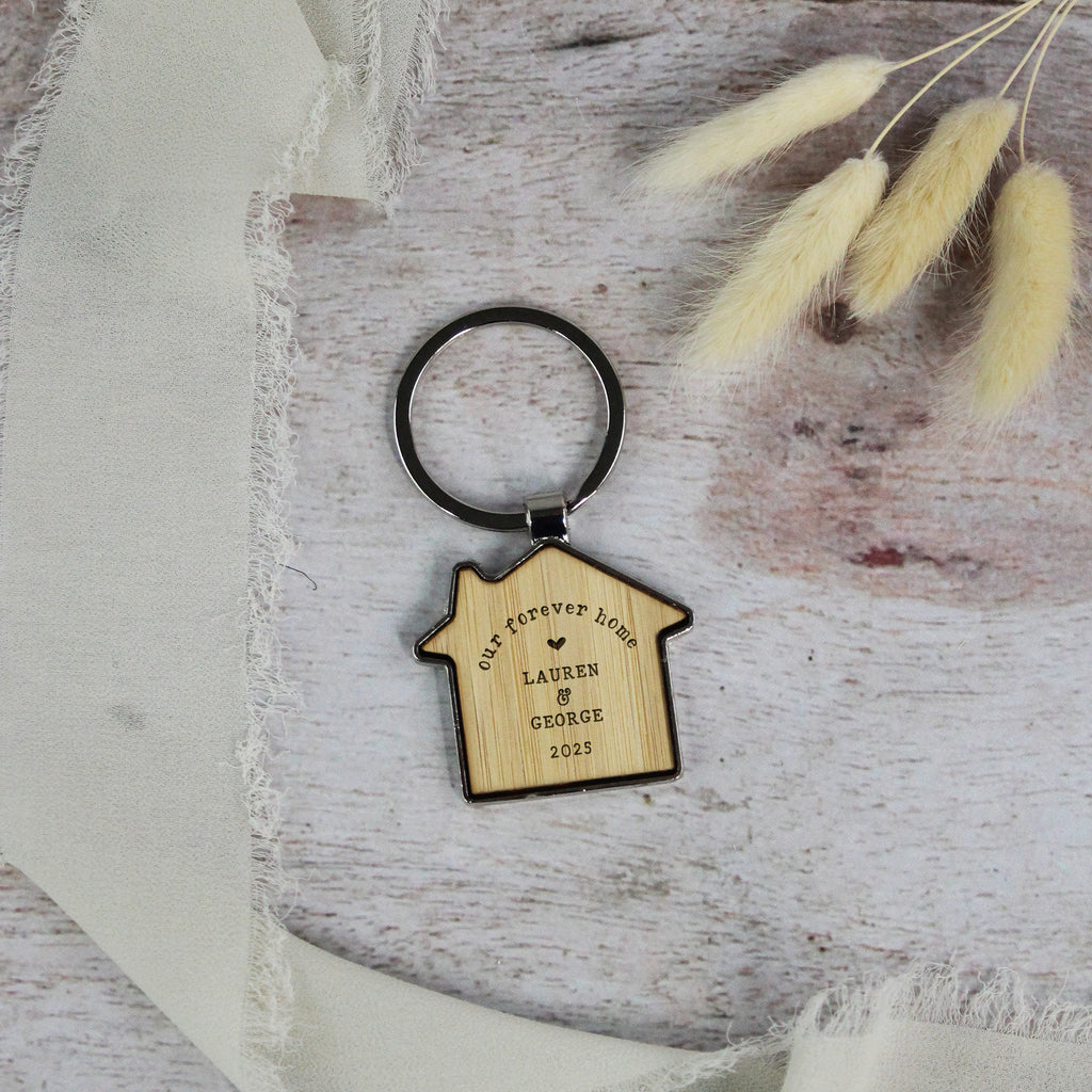Wooden house-shaped keychain with engraved text on a textured surface with dried plants.