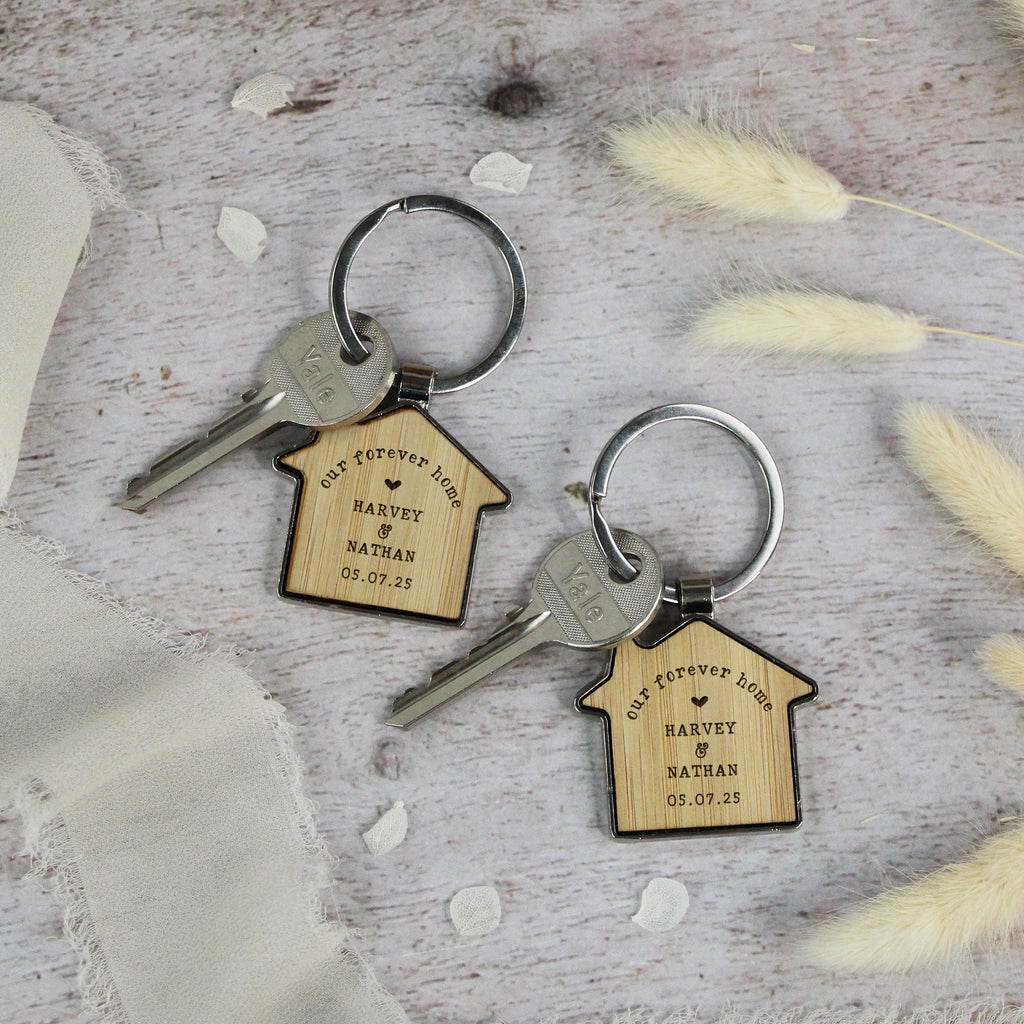 Two wooden house-shaped keychains with engraved text on a rustic surface.