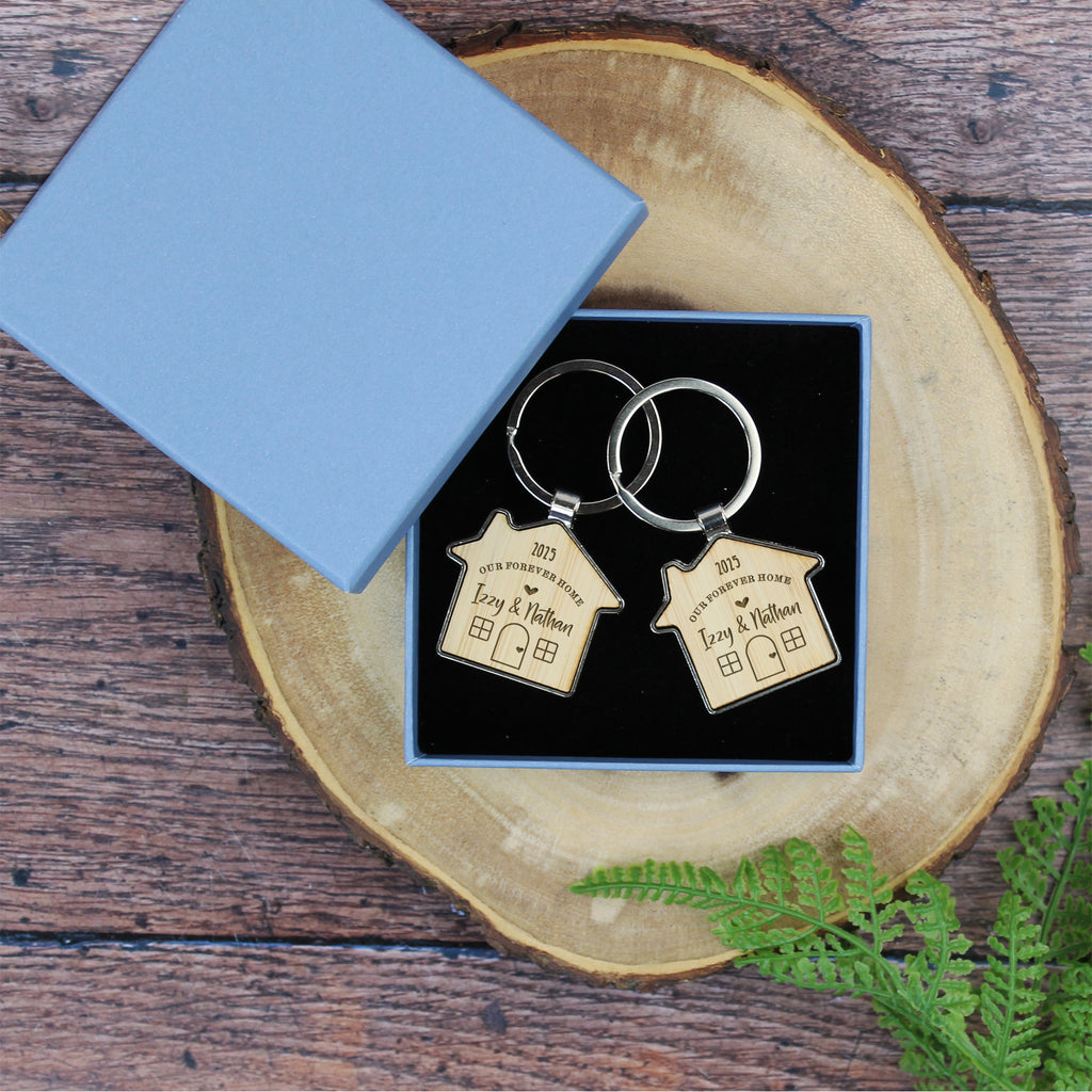 Two house-shaped keychains in a box on a wooden surface with a blue card.