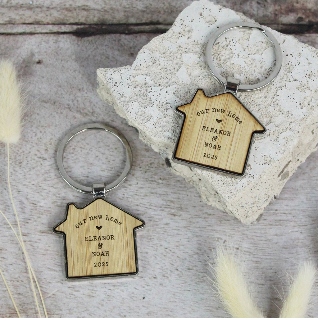 Two wooden house-shaped keychains with engraved text on a stone surface.