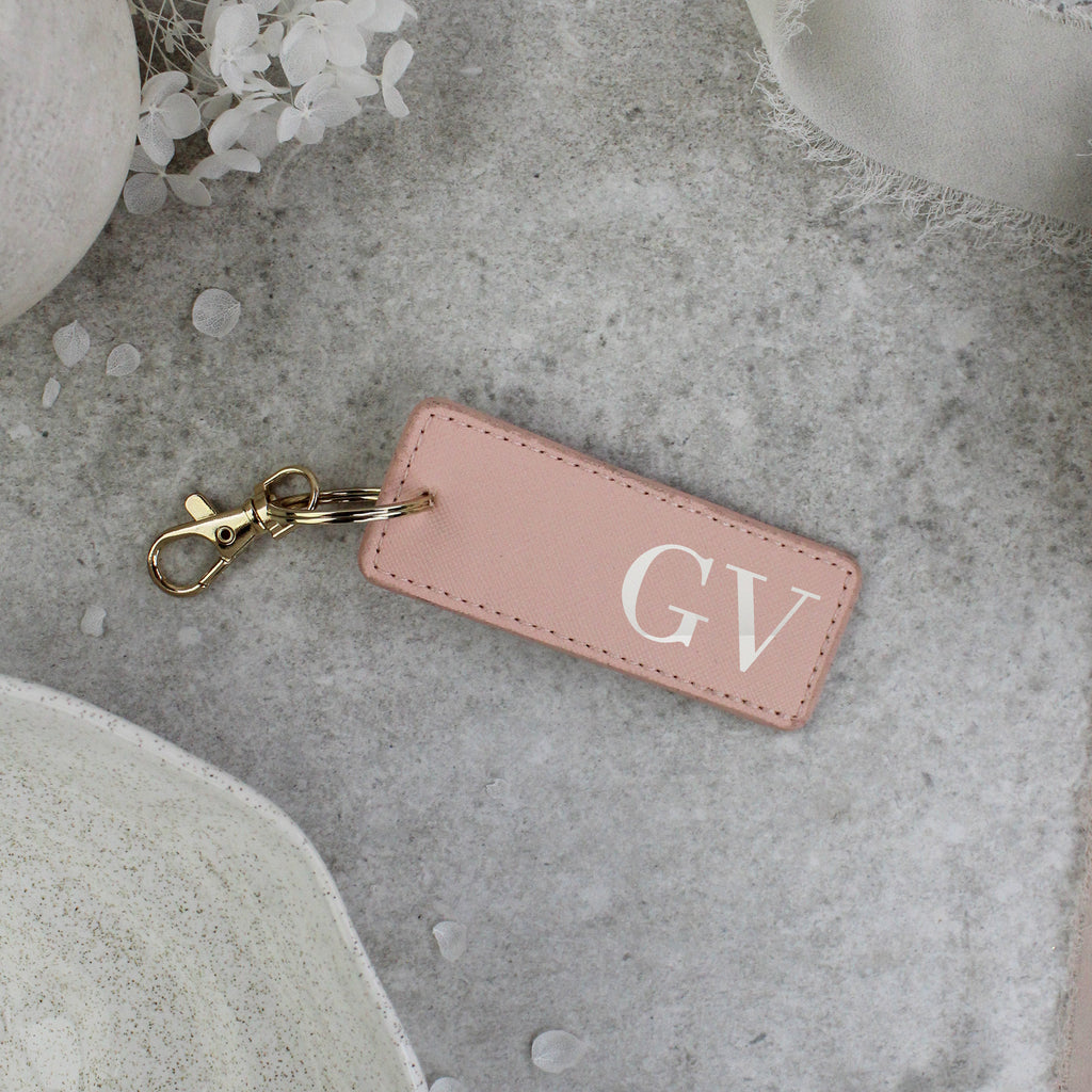 Pink leather keychain with 'GV' initials on a gray surface with decorative elements.