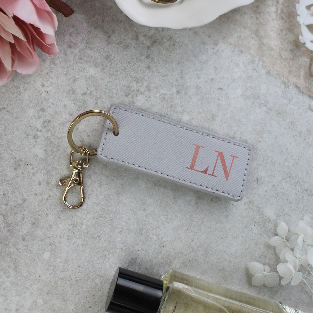 Keychain with 'LN' initials on a textured surface with flowers and a bottle.