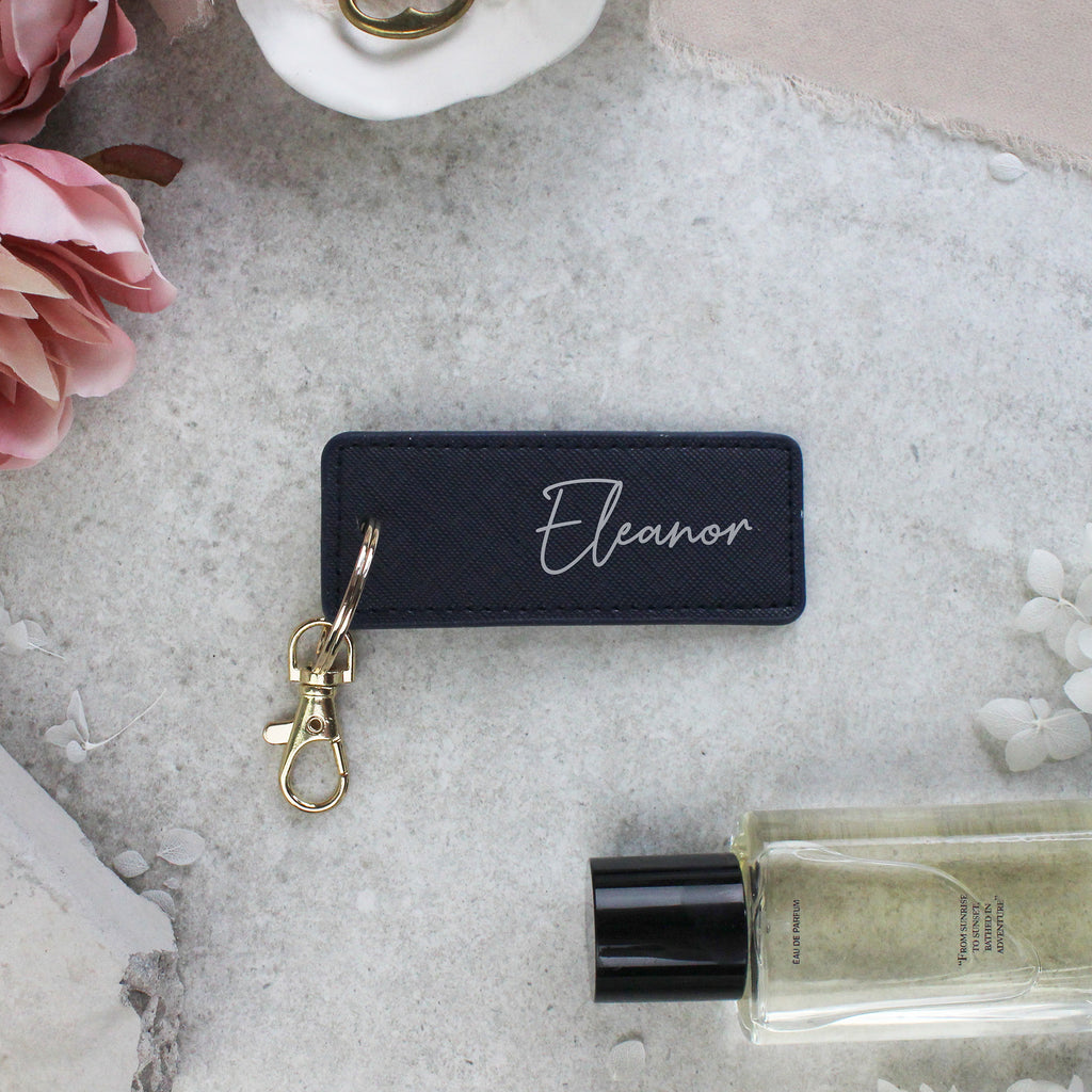 Black keychain with 'Eleanor' engraving on a textured surface with flowers and a bottle.