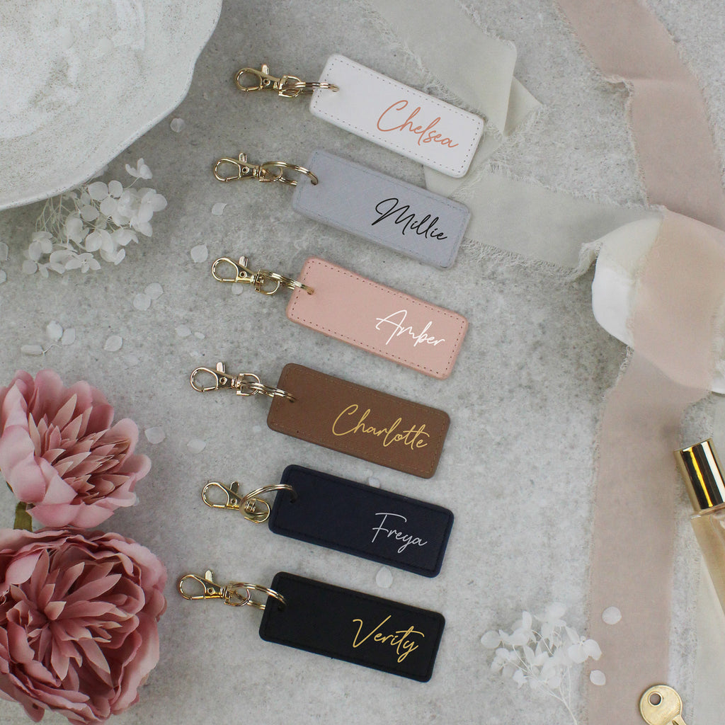 Personalized keychains with names on a soft surface with flowers and a bottle.