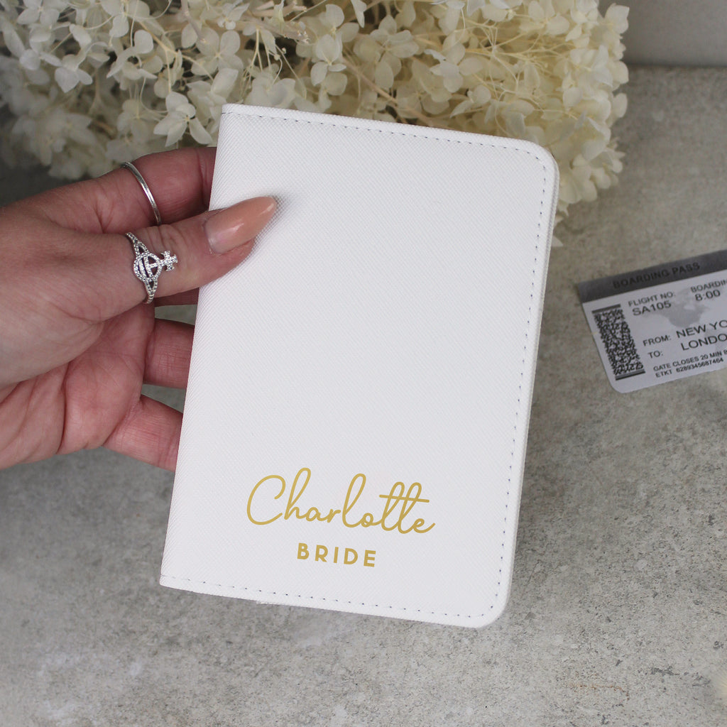 White passport holder with 'Charlotte Bride' text held by a hand, with flowers in the background.
