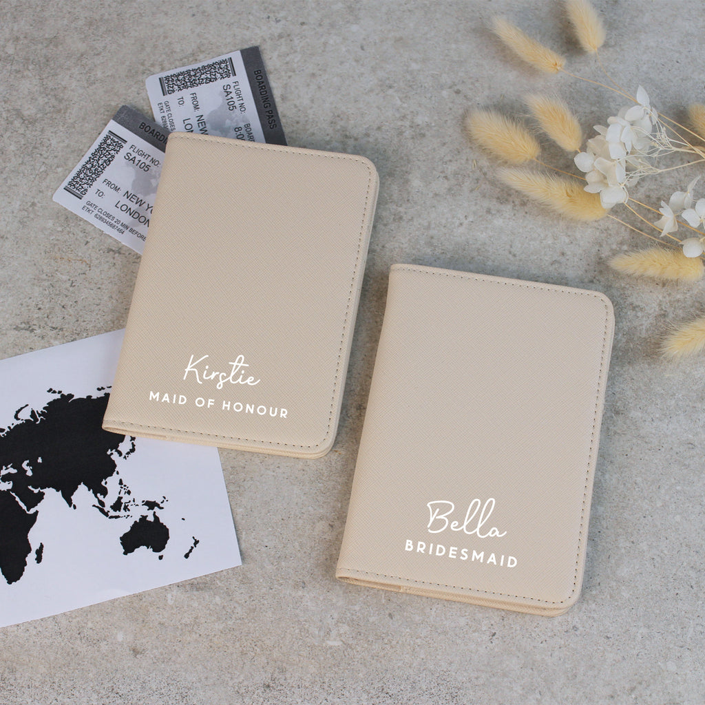 Two beige passport holders with names printed on them, placed on a textured surface with a world map and flowers.