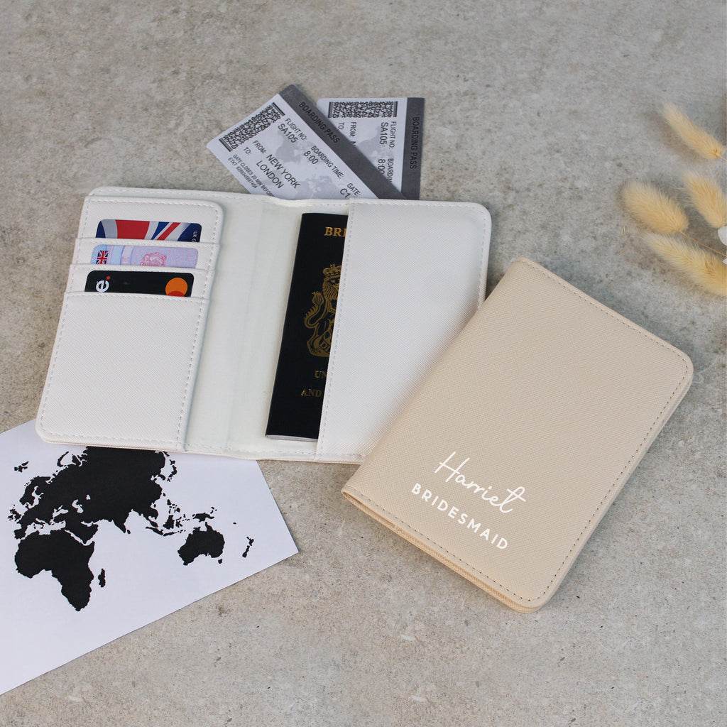 Beige passport holder with 'Harriet Bridesmaid' text, open wallet with cards and passport, world map, and yellow object on gray surface.