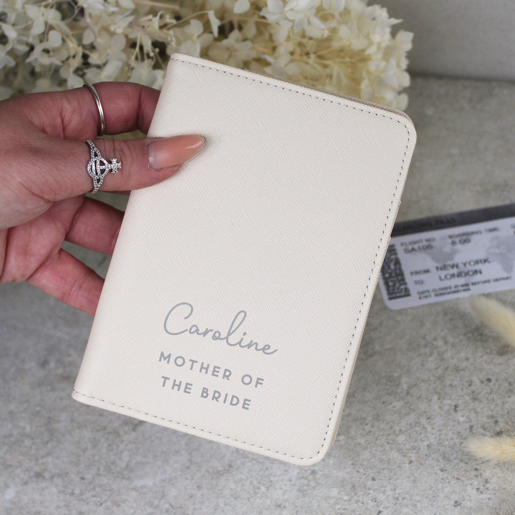 Beige passport holder with 'Caroline Mother of the Bride' text held by a hand.