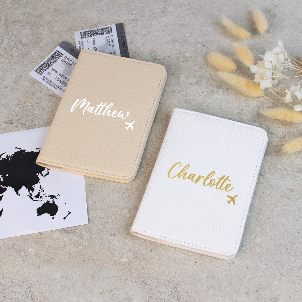 Two personalized passport holders on a concrete surface with travel-related items.