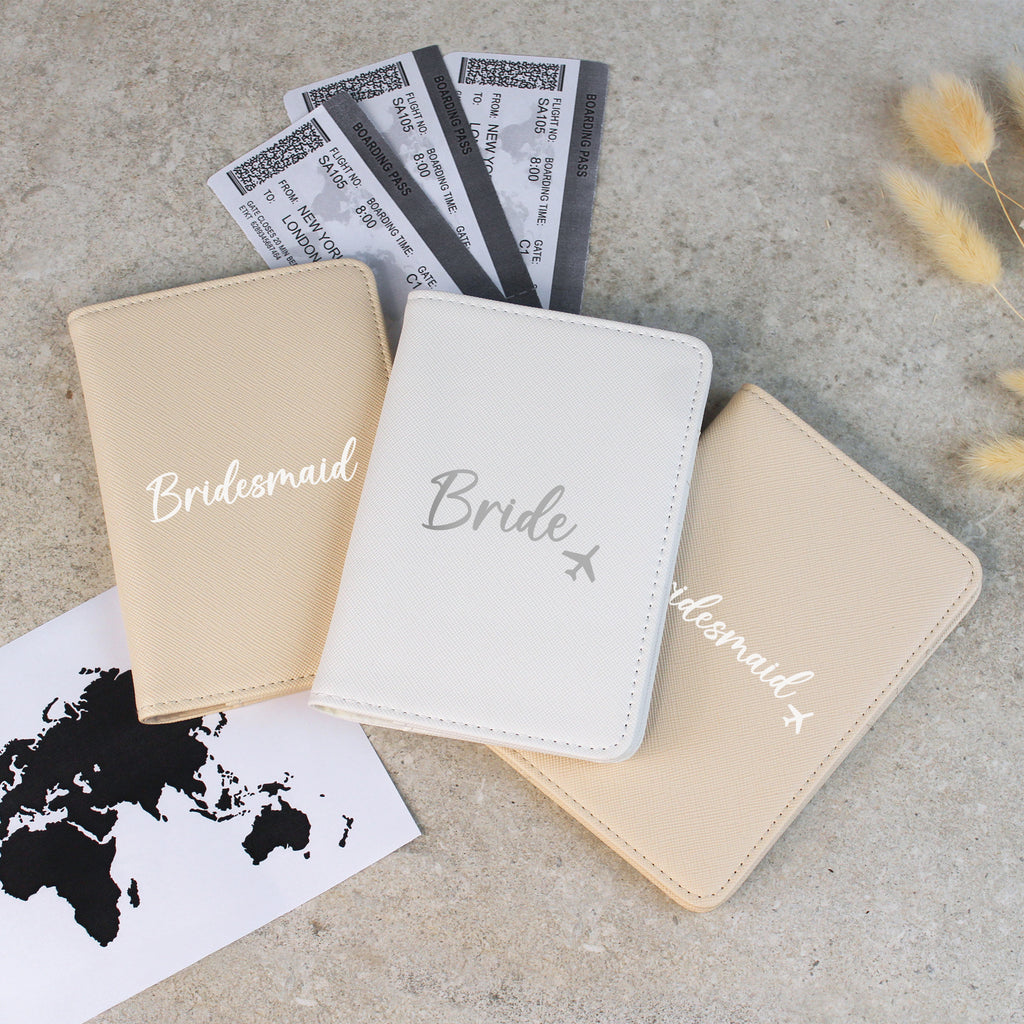 Three passport holders labeled 'Bride', 'Bridesmaid' on a concrete surface with travel-themed items.