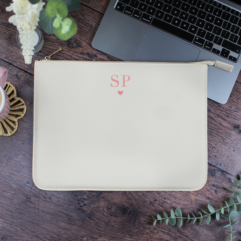 Beige pouch with initials 'SP' on a wooden surface with a laptop and flowers.