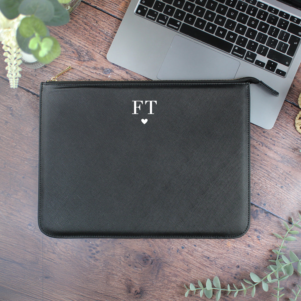 Black pouch with 'FT' initials and a heart on a wooden surface with a laptop.
