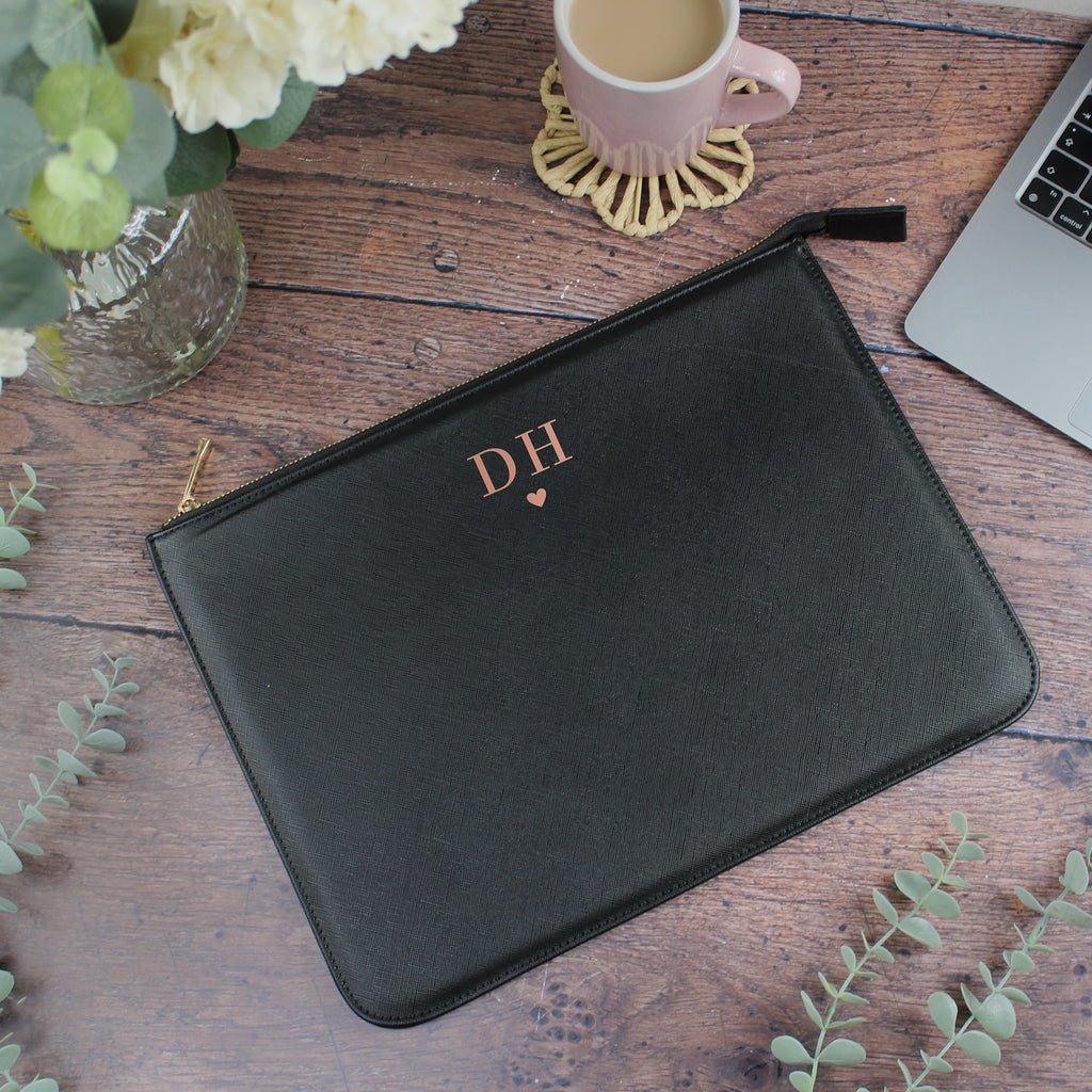 Black pouch with initials 'DH' on a wooden surface with a cup and laptop.